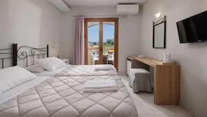 A hotel room with two beds, a desk, a chair, a TV, and a view through a door. - Louvre Hotel (Corfu)
