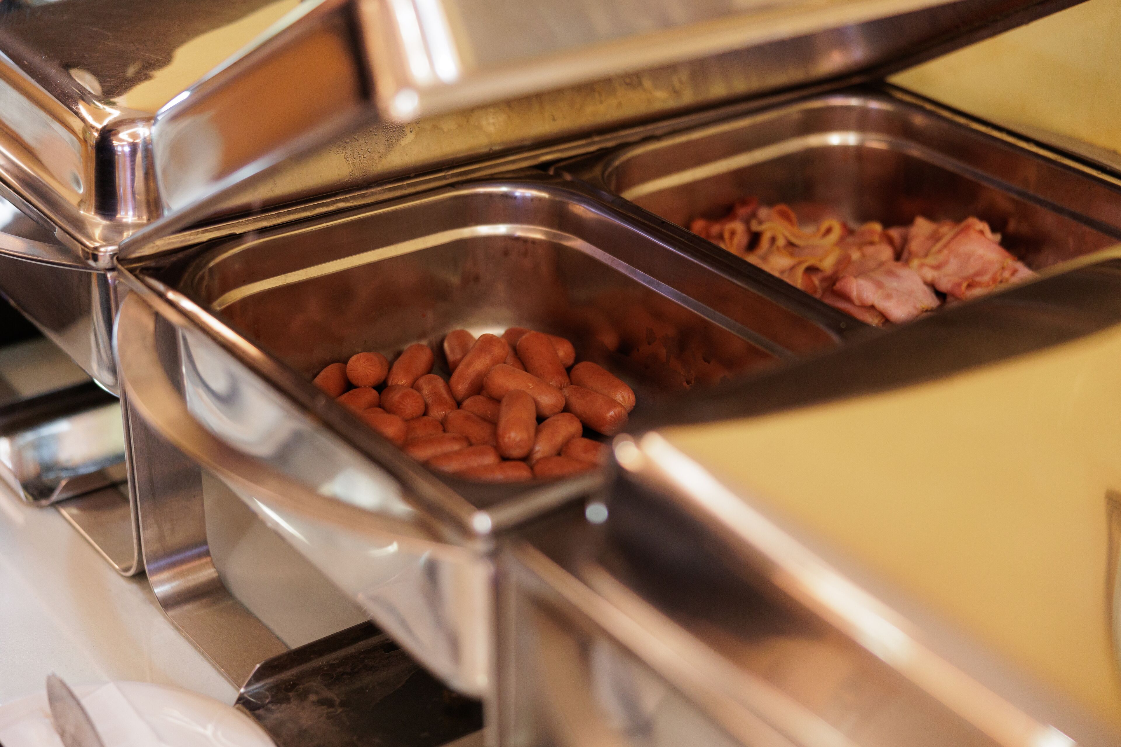 A buffet with various food items including hot dogs and ham.