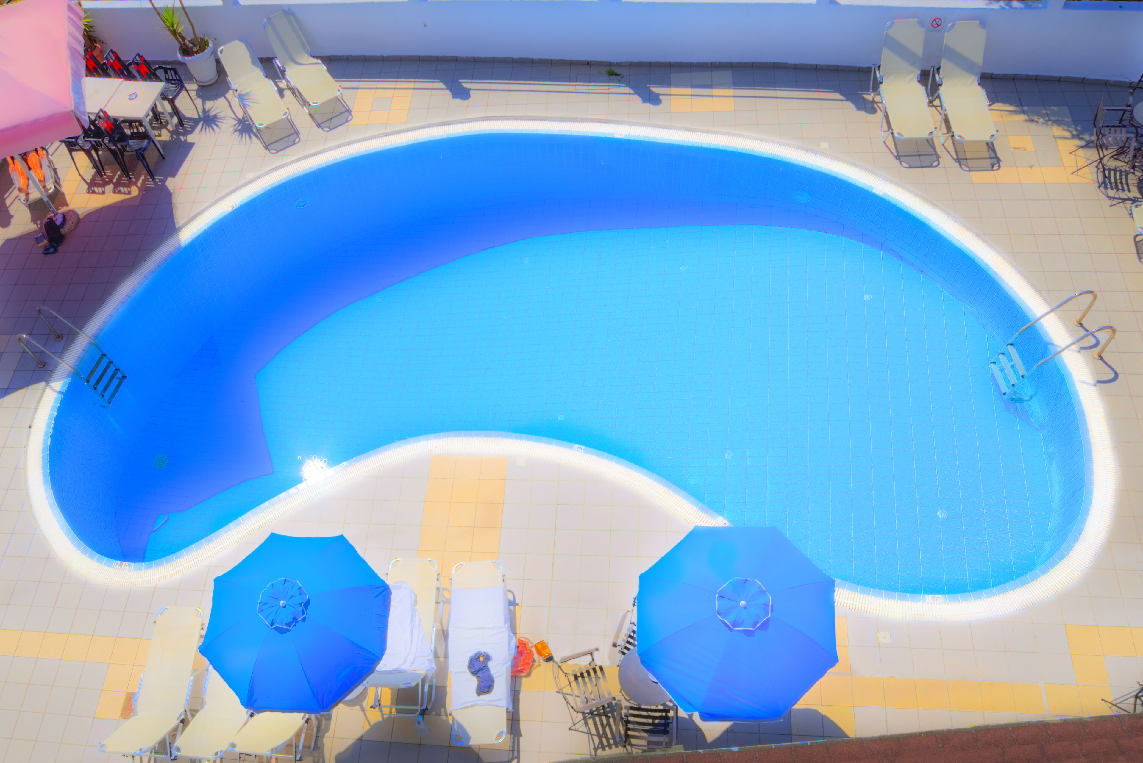 Una grande piscina curvo con lettini e ombrelloni intorno.