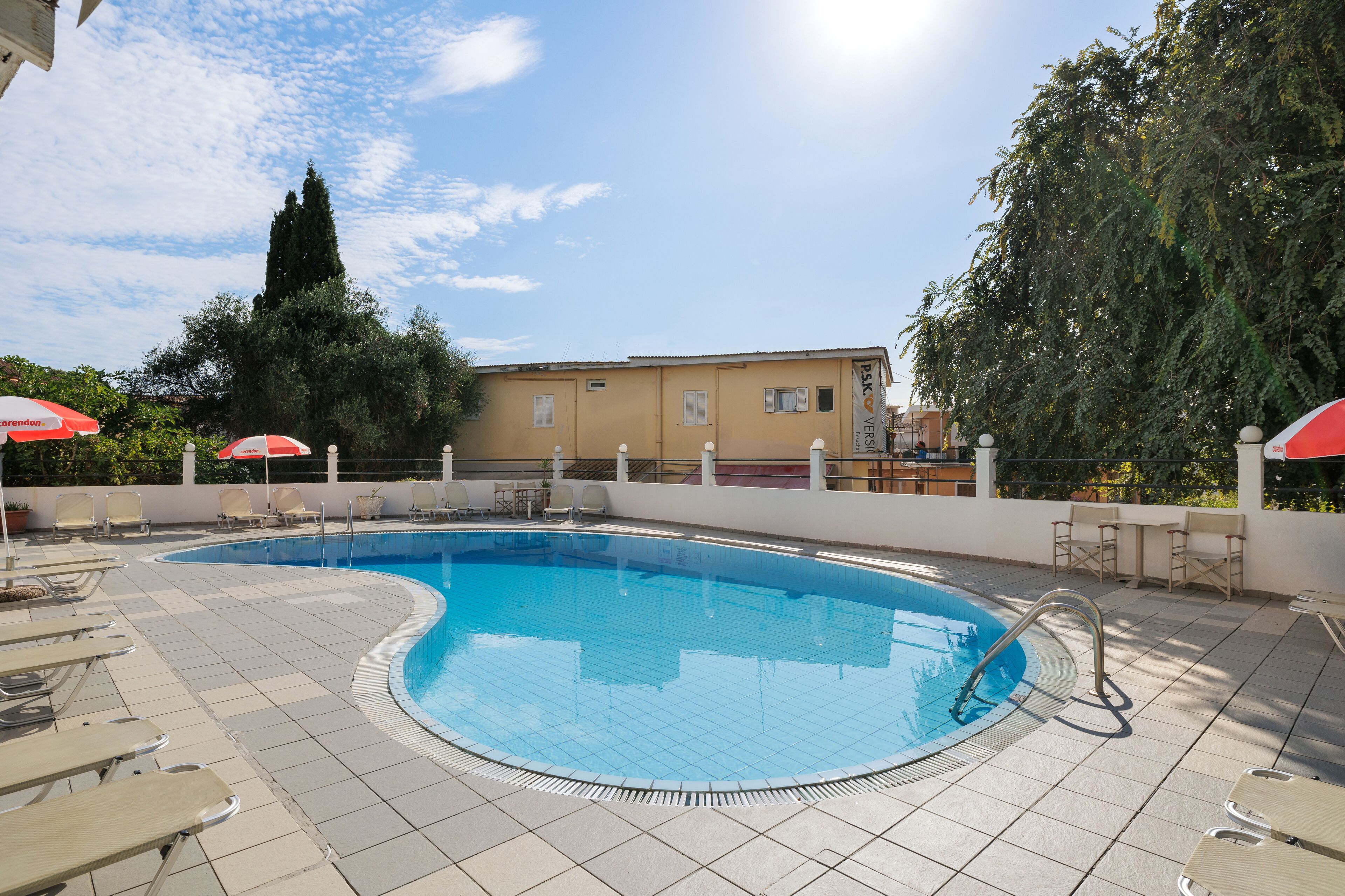 A swimming pool with lounge chairs and umbrellas, surrounded by a tiled deck and trees.