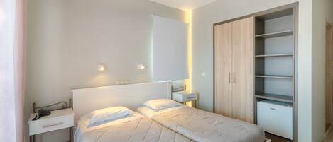 A modern bedroom with a bed, bedside tables, a wardrobe, and a small desk with a telephone.