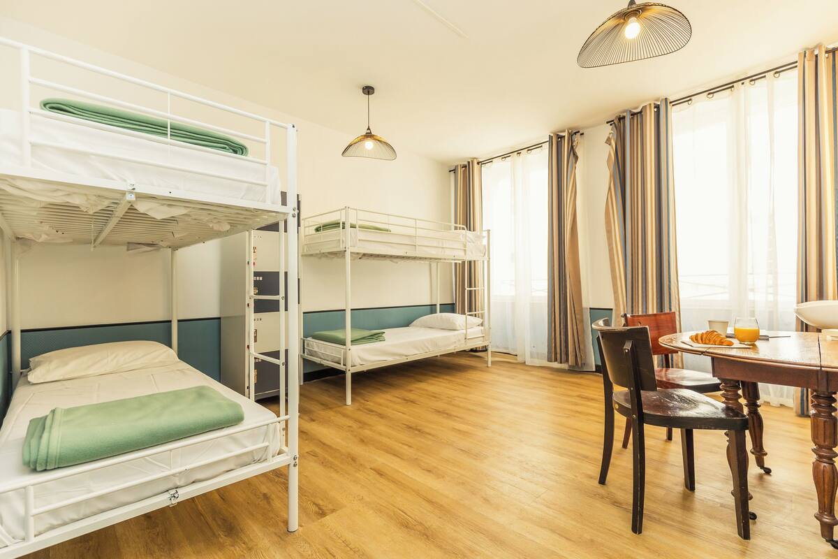 Een kamer met stapelbedden, een eettafel met stoelen en een raam met gordijnen.