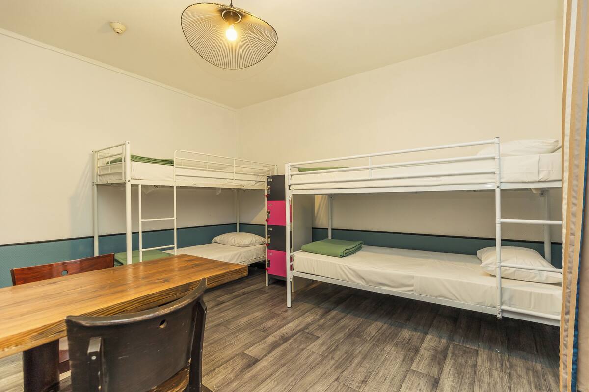 Een slaapzaal met stapelbedden, een houten tafel en een stoel.