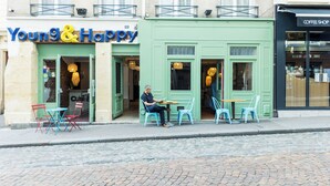 Un café appelé « Young & Happy », avec des tables en terrasse, et un autre café situé de l’autre côté de la rue.