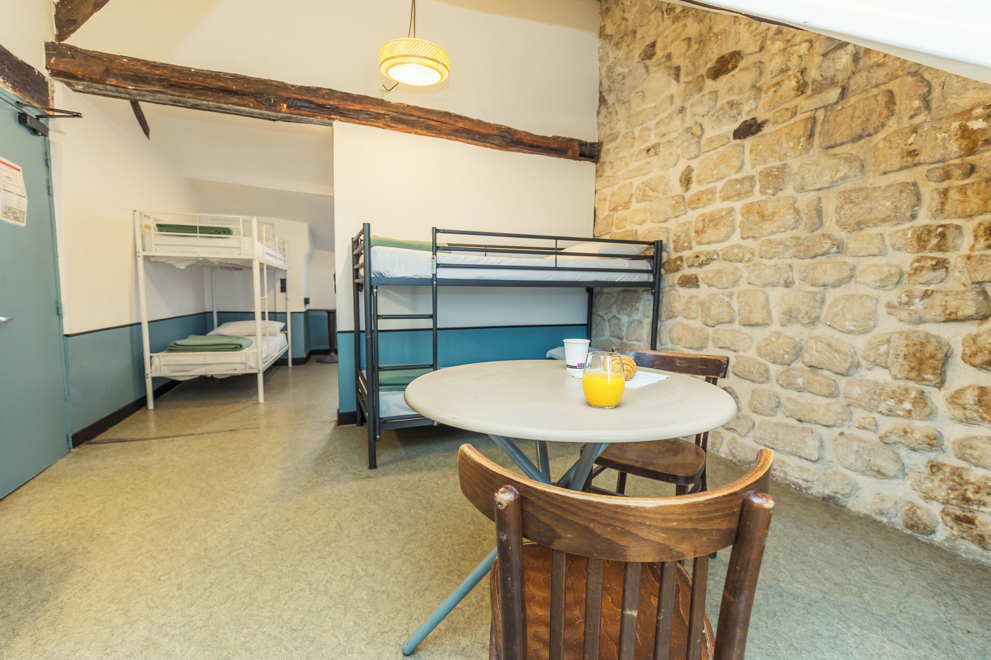 A room with bunk beds, a round table with chairs, a stone wall, and a hanging light fixture.