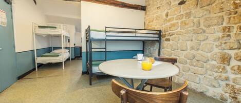 A room with bunk beds, a round table with chairs, a stone wall, and a hanging light fixture.