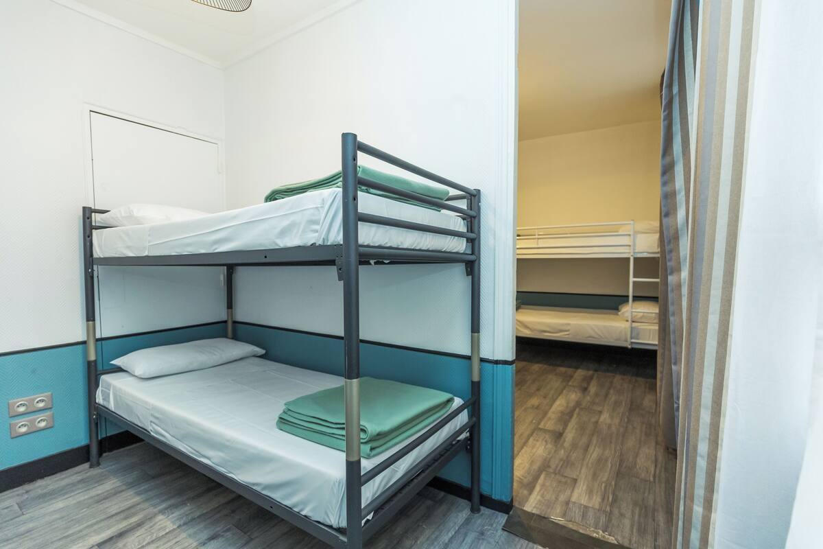 Een slaapkamer met een stapelbed, een houten vloer, een witte deur en een raam.