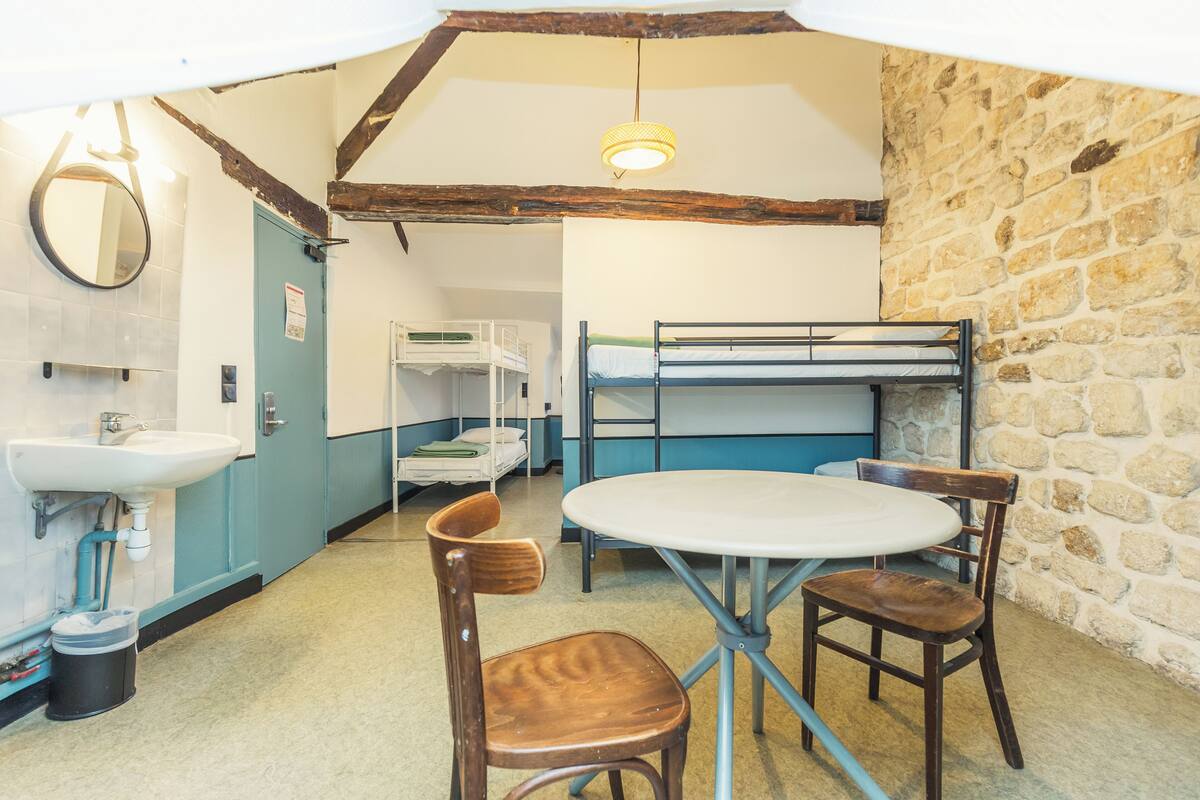 Een kamer met stapelbedden, een wastafel en een ronde tafel met stoelen.