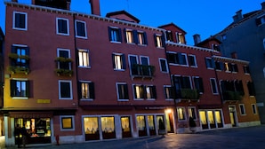 A row of red buildings with multiple windows and balconies, some with plants. - Palazzo del Giglio (Venice)
