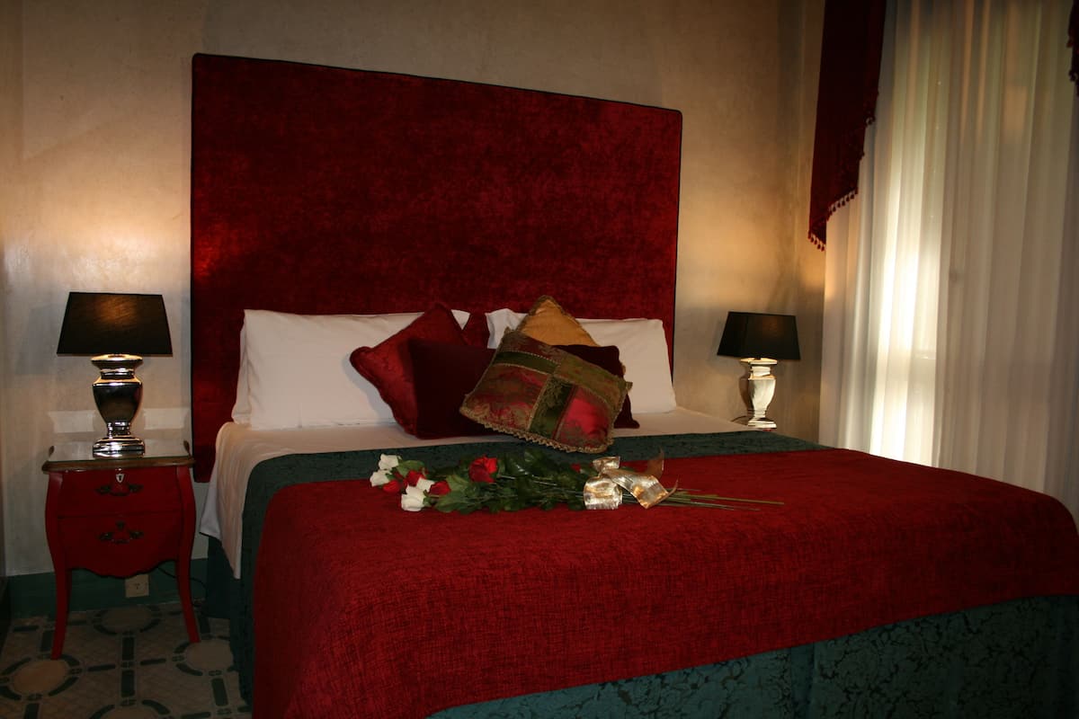 Une chambre d’hôtel avec un grand lit, une literie rouge, deux lampes de chevet et un bouquet de fleurs posé sur le lit.