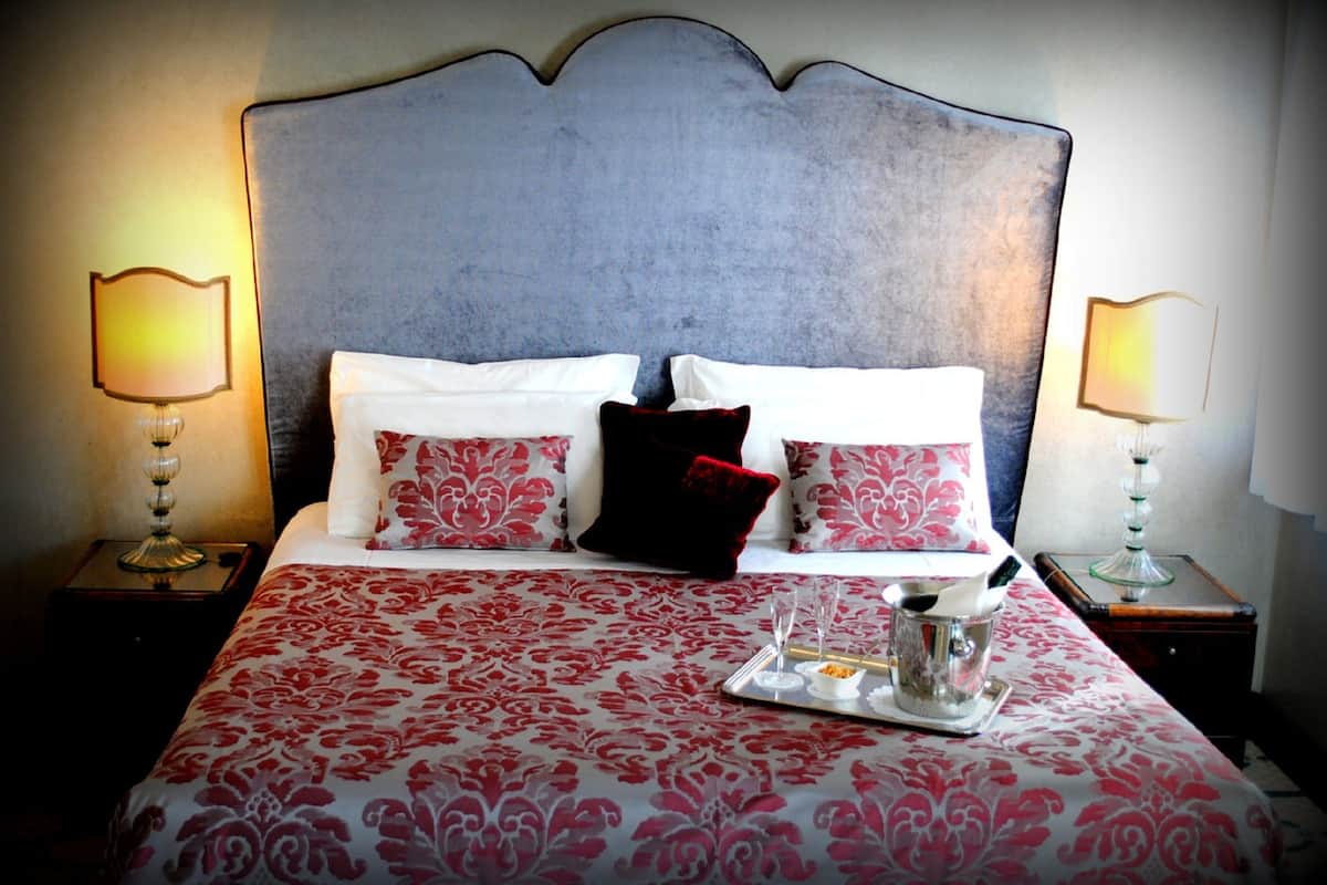 Un lit bien fait, recouvert d’une couvre-lit à motifs, avec deux lampes de chevet et un plateau contenant une carafe et des bols posé sur la table de chevet.