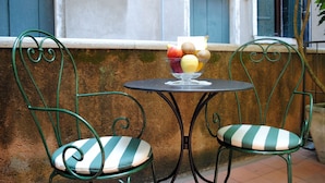 A small outdoor seating area with two chairs and a table, a bowl of fruit, and a window with blue shutters. - Palazzo del Giglio (Venice)