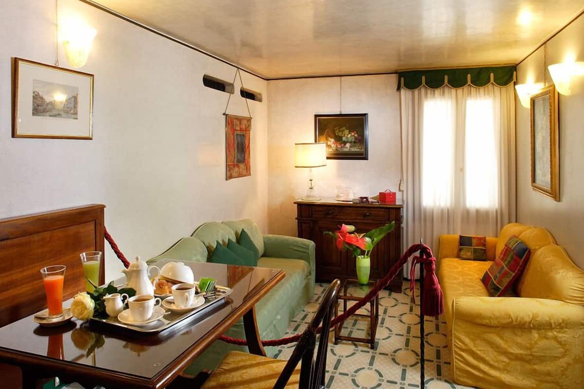 Une chambre d’hôtel avec une table à manger dressée pour le petit-déjeuner, un canapé vert, un canapé jaune et un petit meuble en bois.
