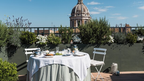 An outdoor dining area with a table set for two, surrounded by greenery and a view of a historical building. - Residenza Napoleone III (Rome)