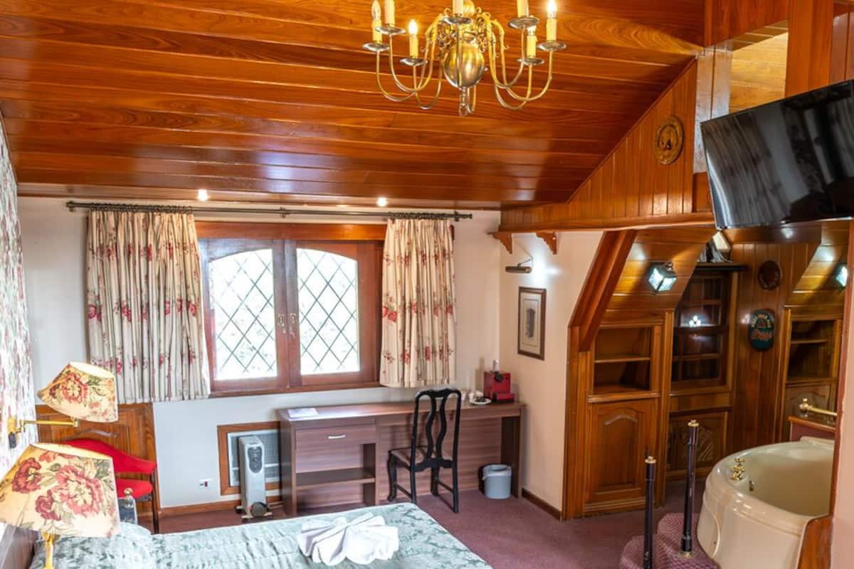 A cozy room with a wooden ceiling, a desk with a chair, a bed with a patterned bedspread, and a television mounted on the wall.