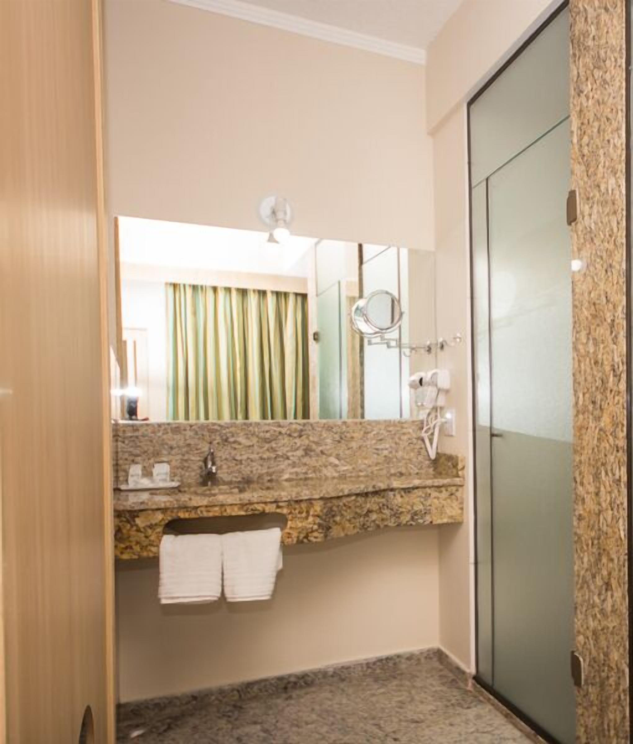 A bathroom with a granite countertop, a mirror, a towel rack, and a shower area.