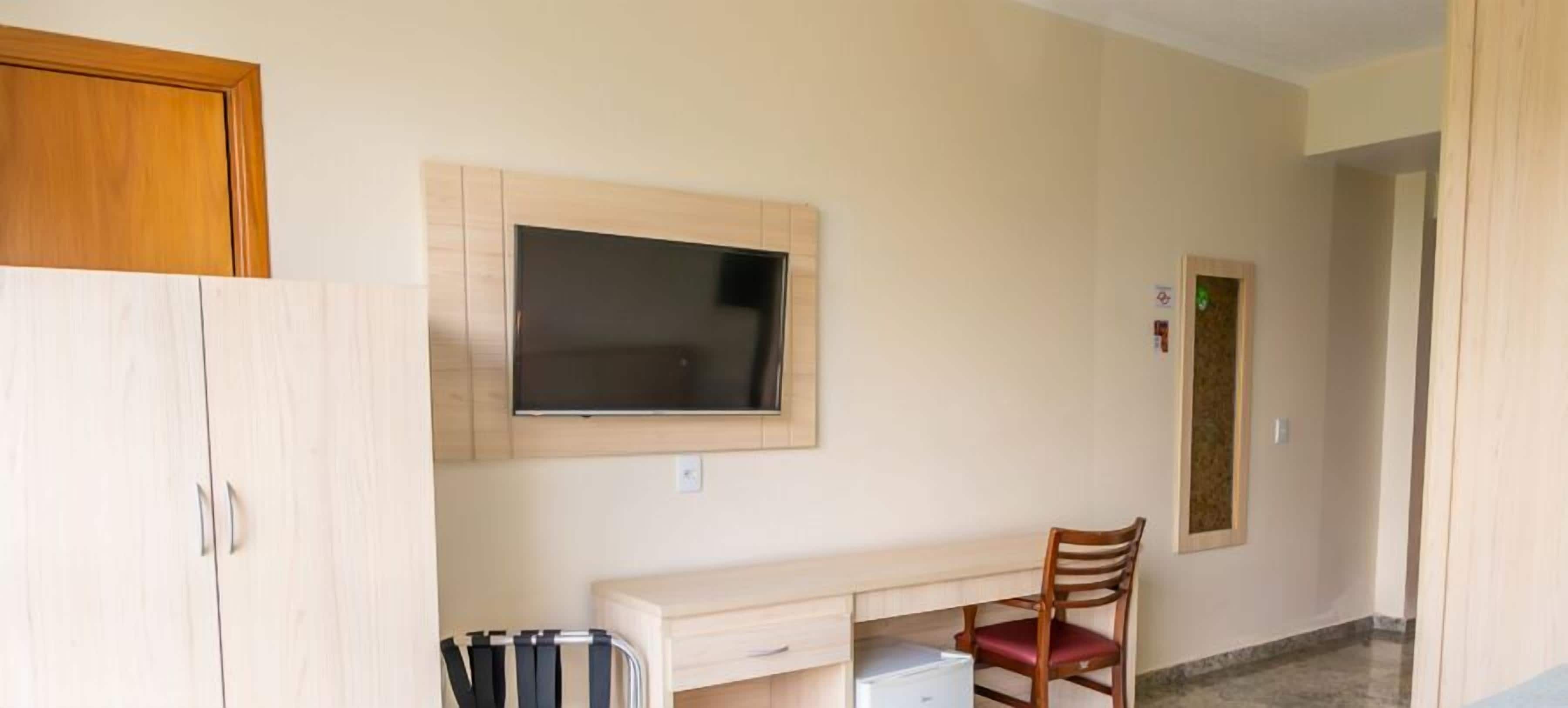 A room with a TV mounted on the wall, a desk with a chair, and a cabinet.