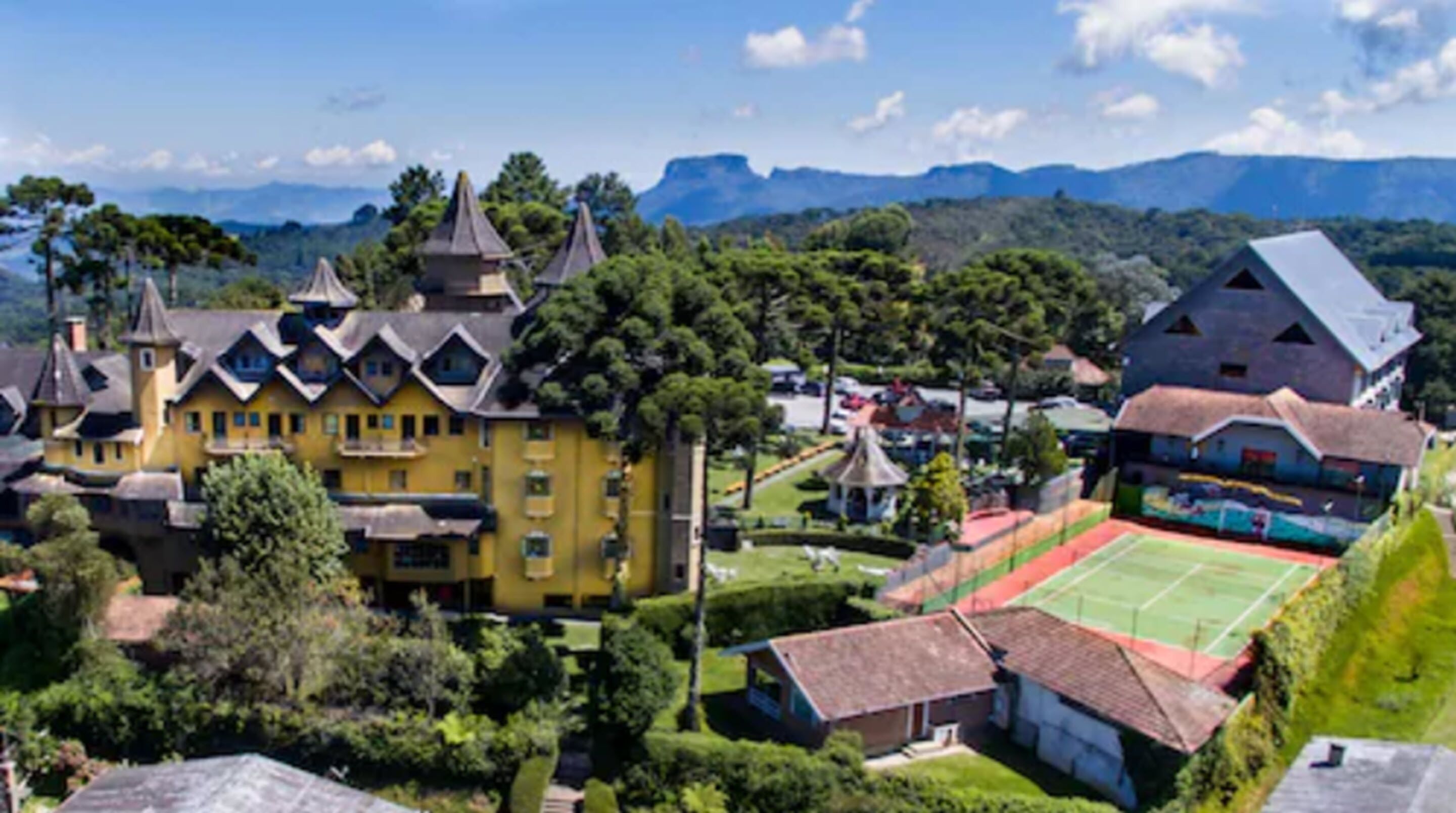 A large yellow building with multiple towers and a tennis court in the foreground.