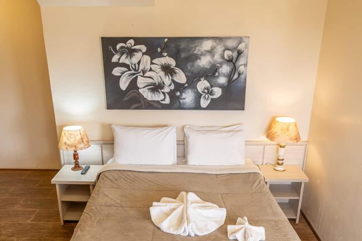 A hotel room with a bed, two bedside tables, a painting of flowers on the wall, and a door.