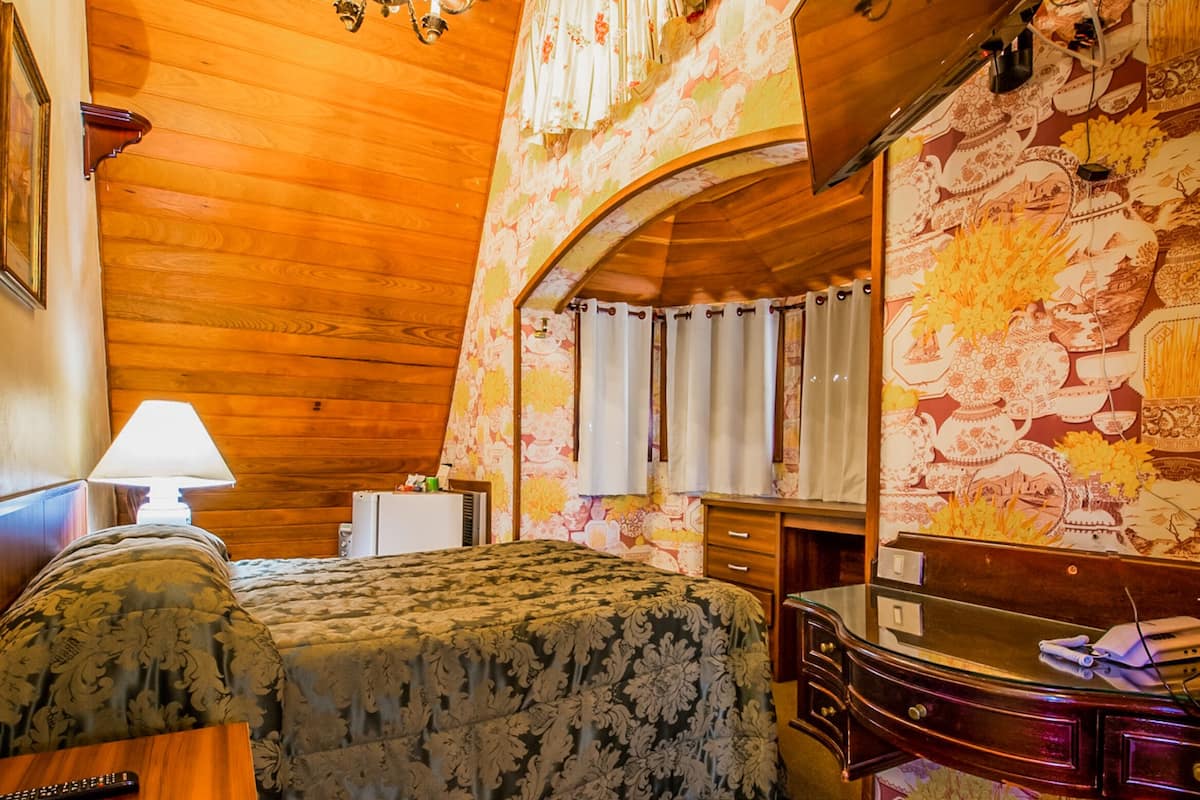A bedroom with a wooden ceiling, a chandelier, a bed with floral bedding, a dresser, a mirror, and a television mounted on the wall.