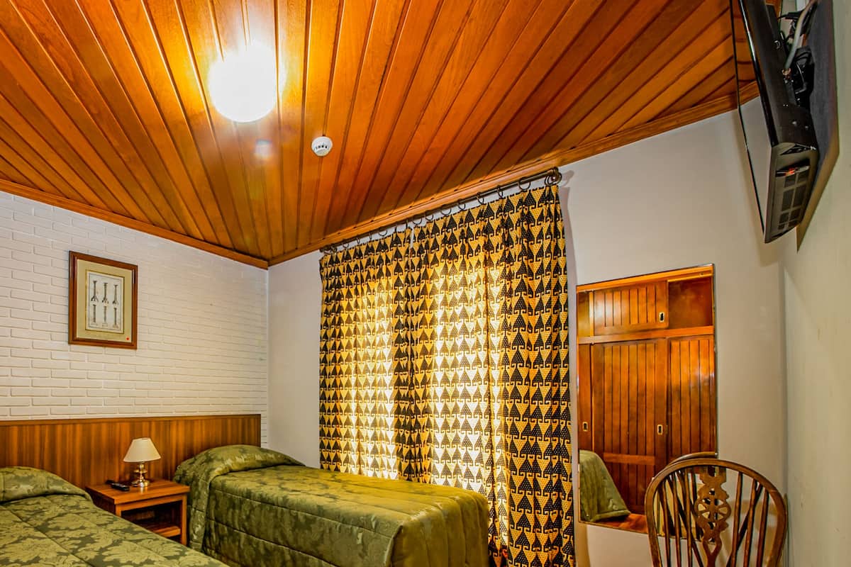 A room with two beds, wooden ceiling, white brick wall, and a patterned curtain.