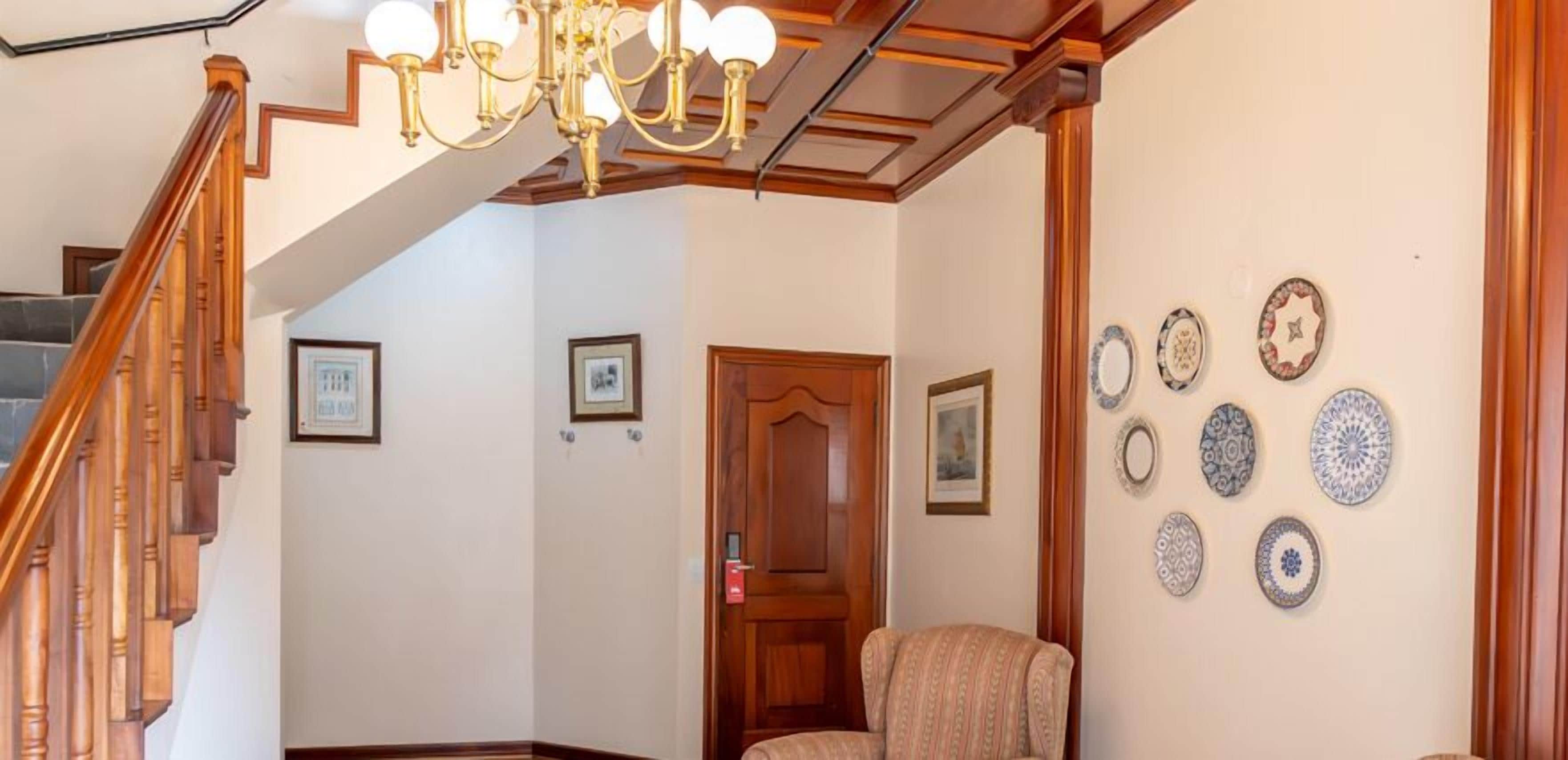 A staircase with wooden railings, a chandelier, and a wall decorated with plates.