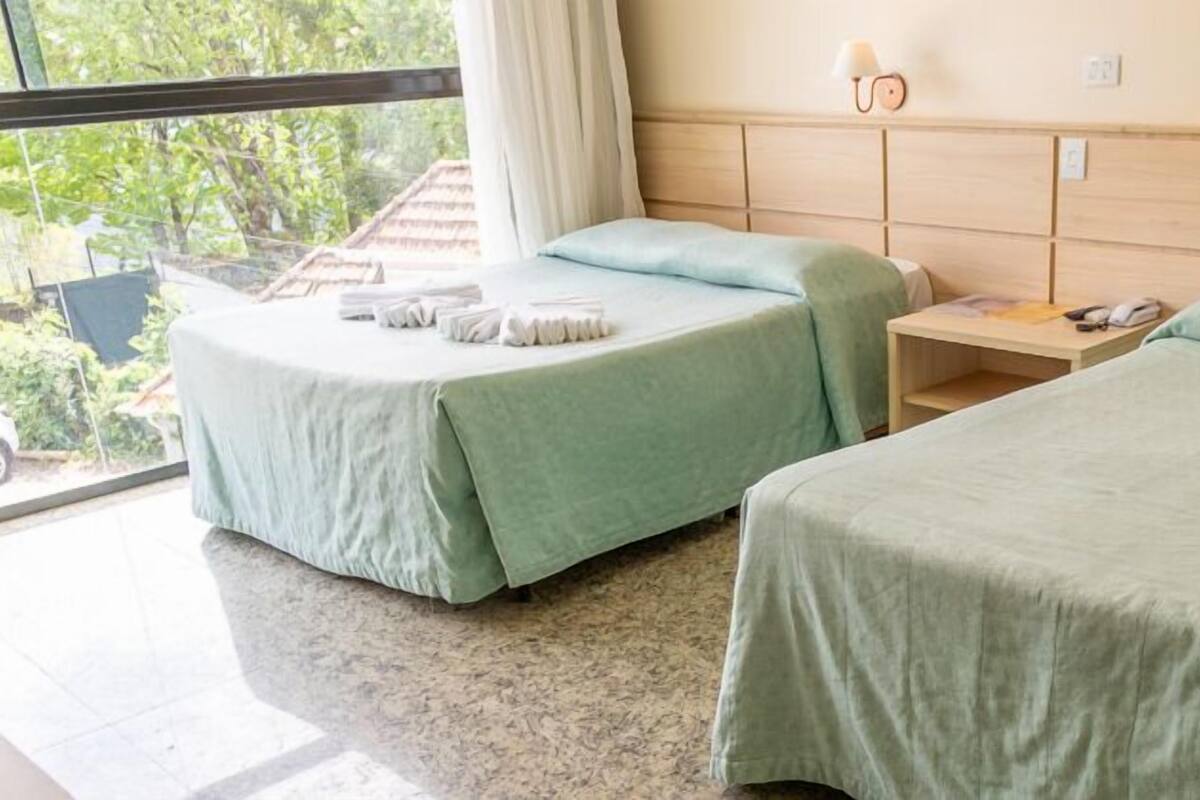 A hotel room with two beds, a small table, and a nightstand.