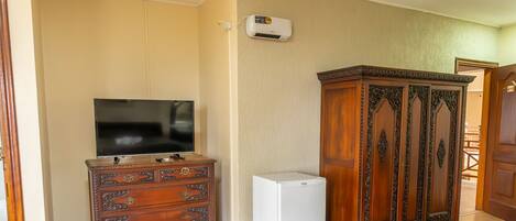 A room with a TV on a wooden dresser, a white refrigerator, and a wooden cabinet.