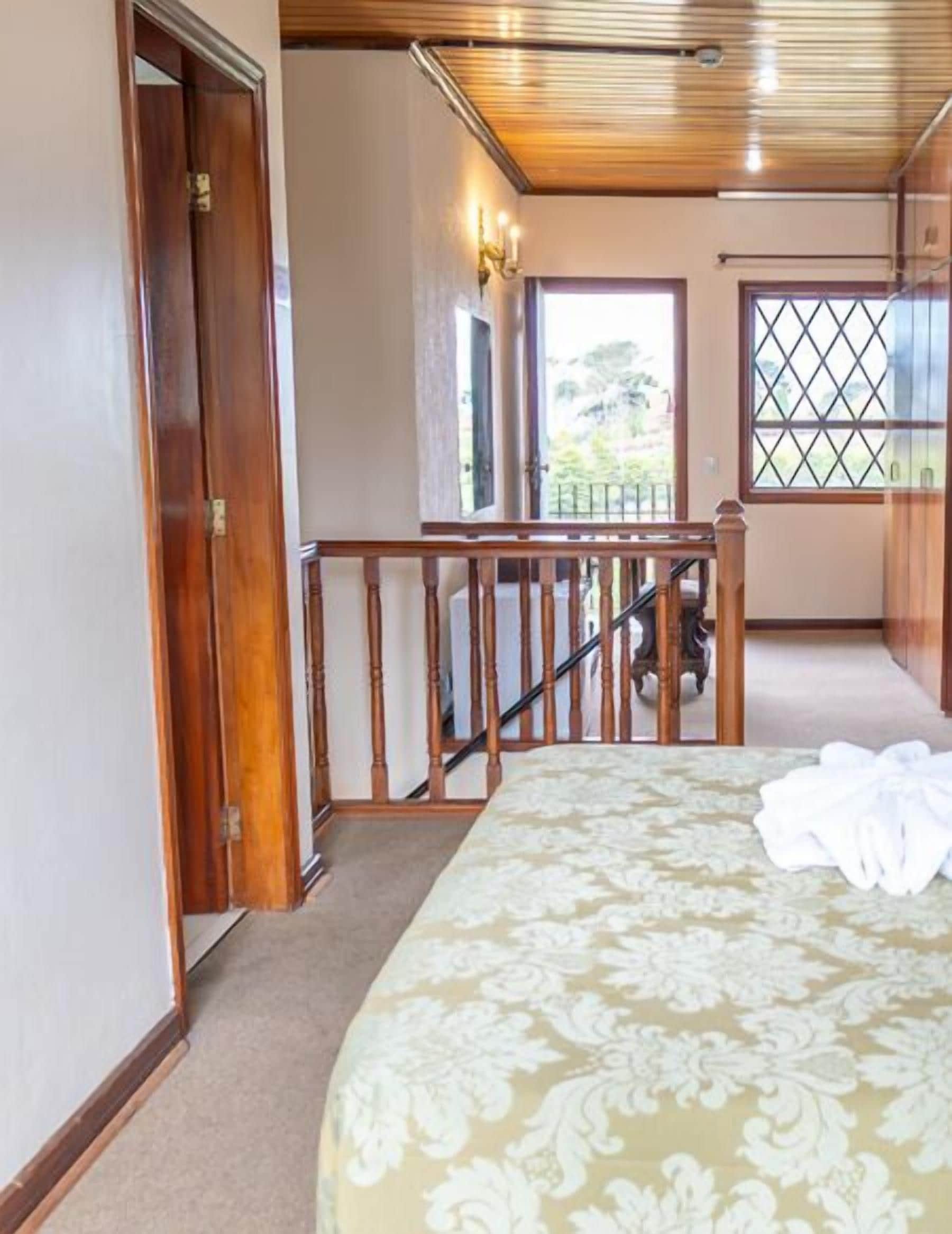 A bedroom with a bed, a wooden staircase, a window with a view, and a door.
