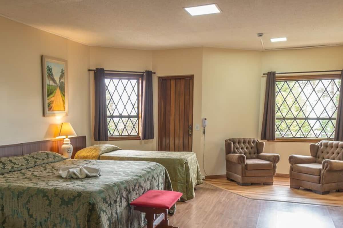 A hotel room with two beds, a dining table, a chair, and a window with curtains.
