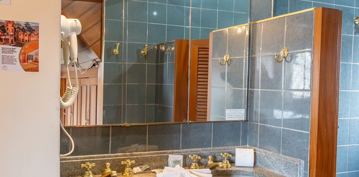 A bathroom with a large mirror, a hairdryer, and a sink with gold faucets.