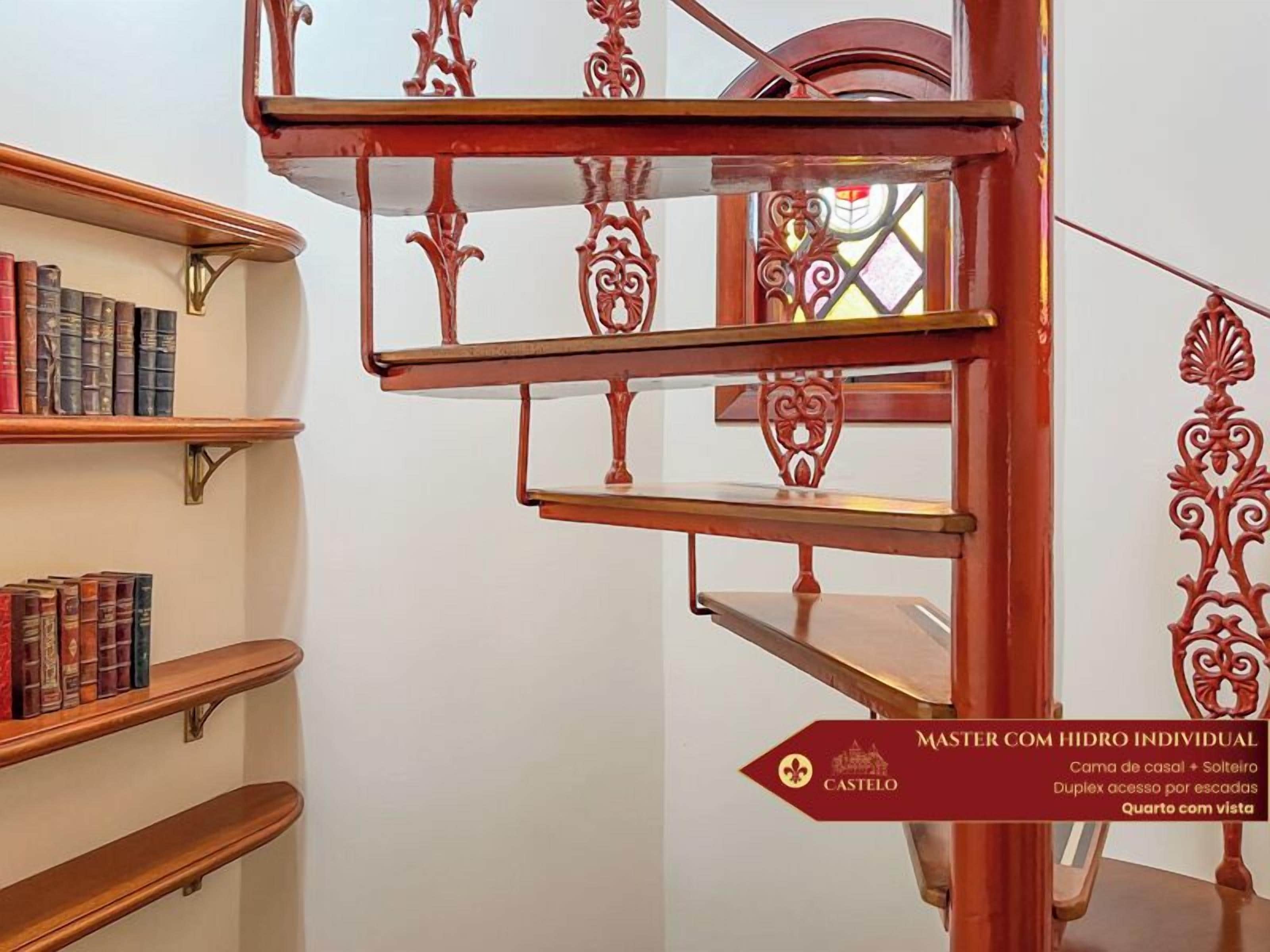 Escadaria com grades de metal ornamentadas e um aviso indicando uma suíte principal com banheiro privativo, acesso duplex por escadas e um quarto com vista.
