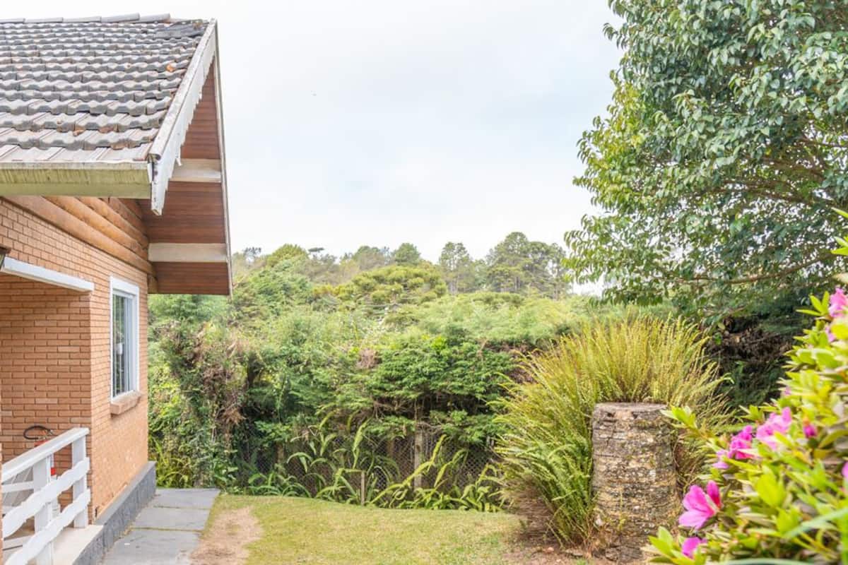 A brick house with a tiled roof, a white bench, and a garden with various plants and flowers.