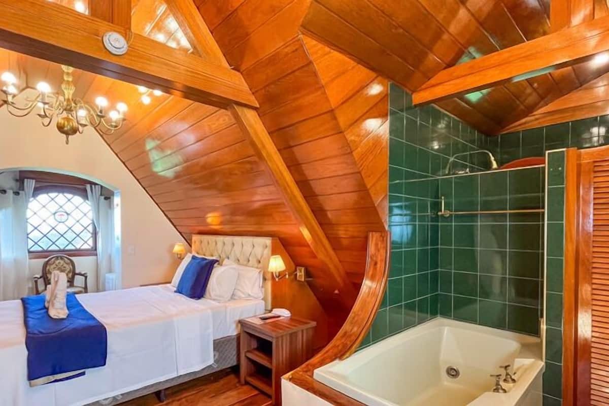 A bedroom with a large bed, a nightstand, a chandelier, and a view of the outside through a window.