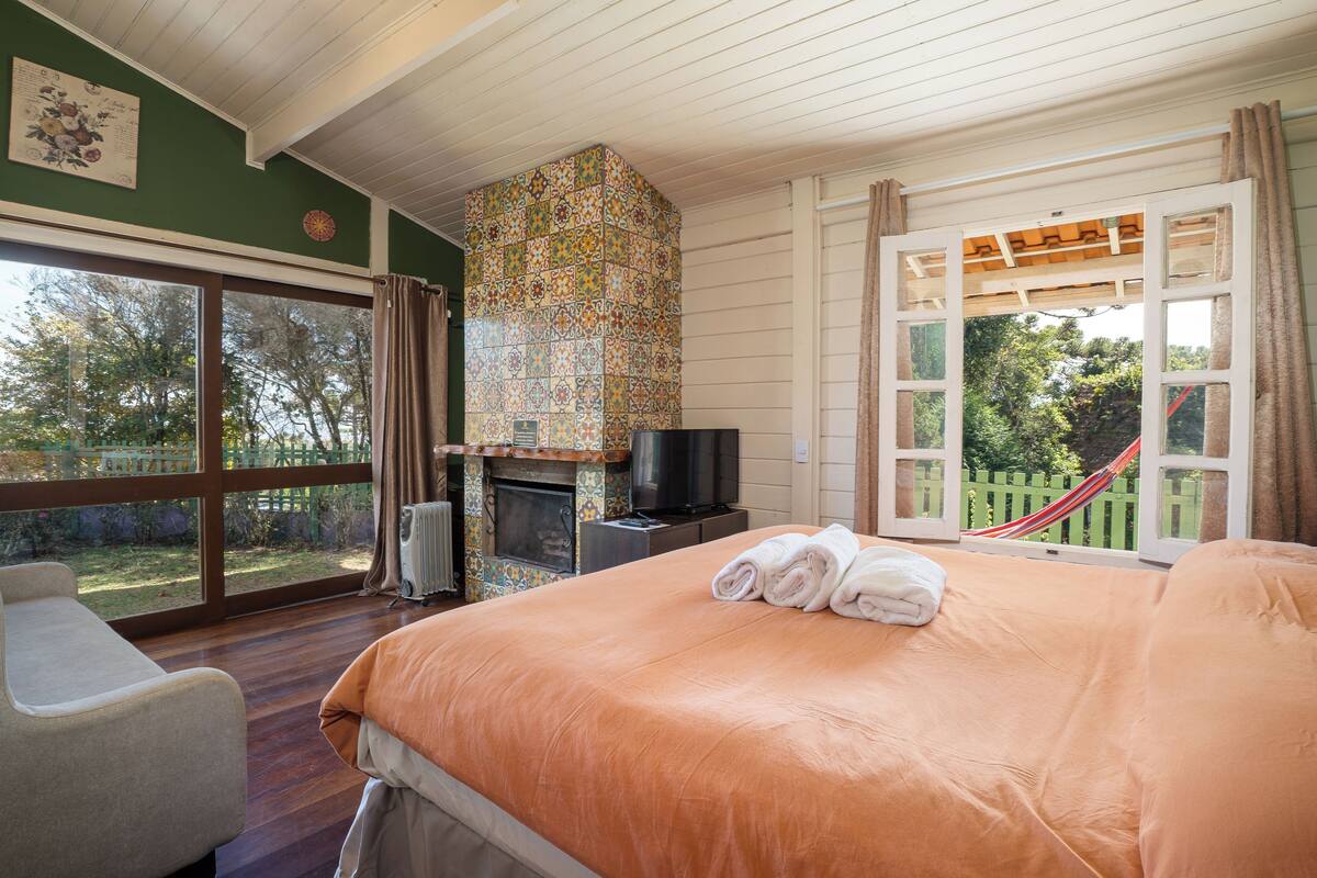 A bedroom with a large bed, a television, a fireplace, and a view of the outdoors.