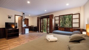 A bedroom with a large bed, a TV, a desk, and a window with a view of trees.
