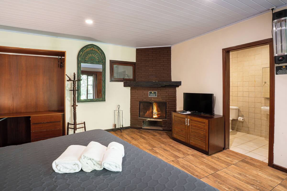 A hotel room with a bed, a wooden wardrobe, a television, a fireplace, and a bathroom.