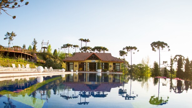 A pool with a reflection of a building and trees, surrounded by lounge chairs and a well-maintained lawn.