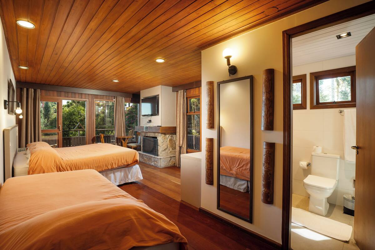 A hotel room with two beds, a fireplace, a TV, and a bathroom with a toilet and shower.