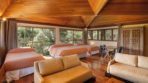 A spacious room with wooden ceilings, two beds, a sofa, and a dining area with a view of trees.