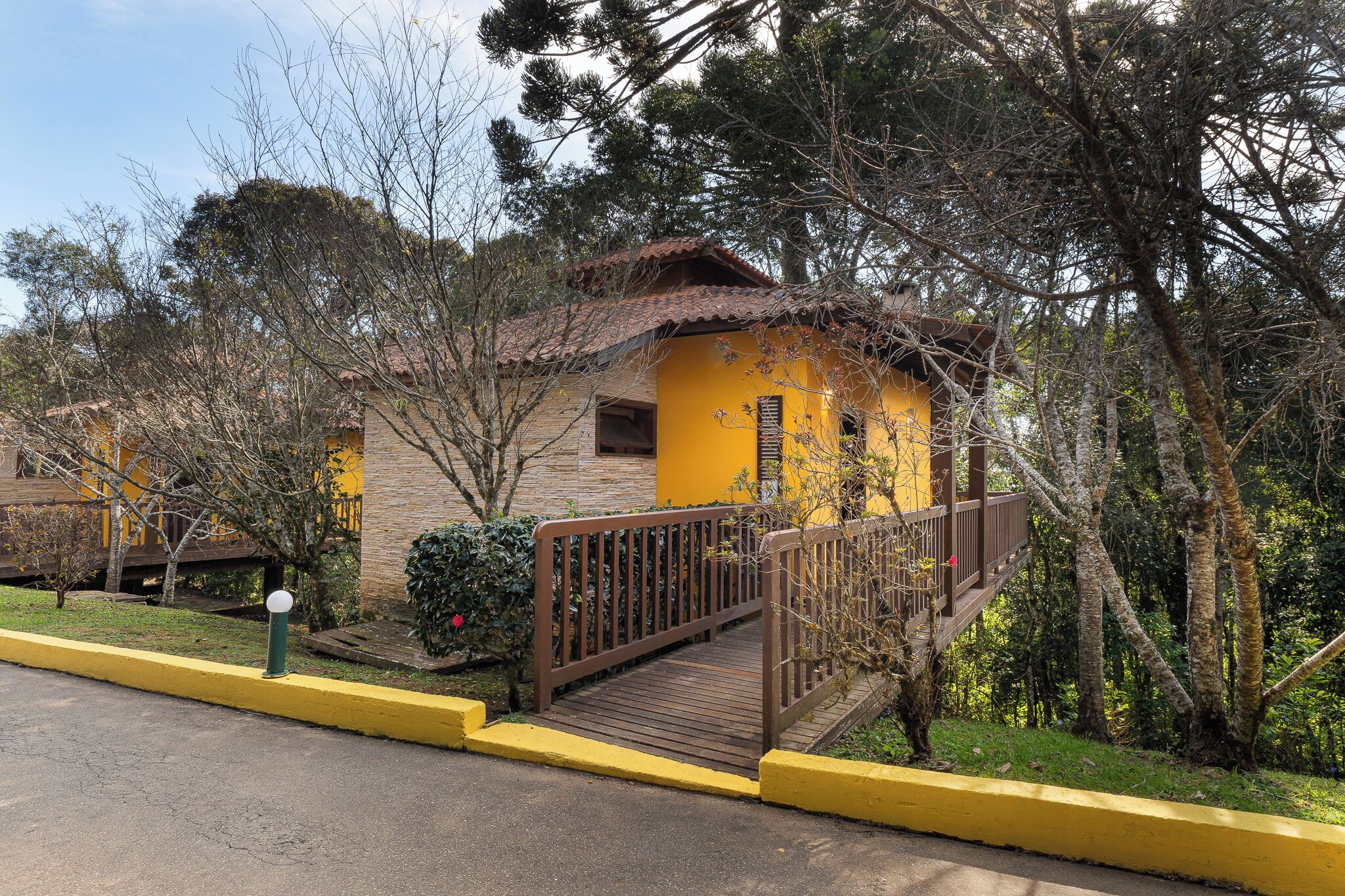 Un bâtiment jaune doté d’une terrasse en bois et d’un pont menant à une structure également en bois.