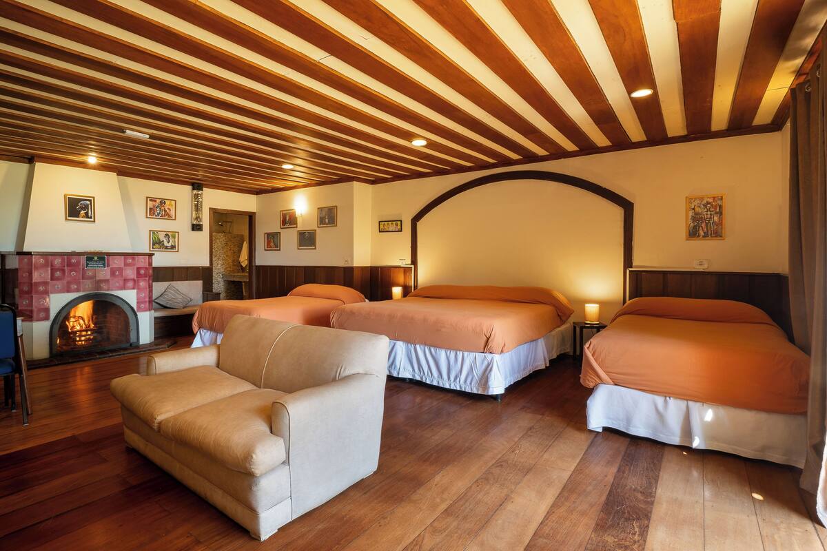 A hotel room with two beds, a sofa, a fireplace, and wooden flooring.