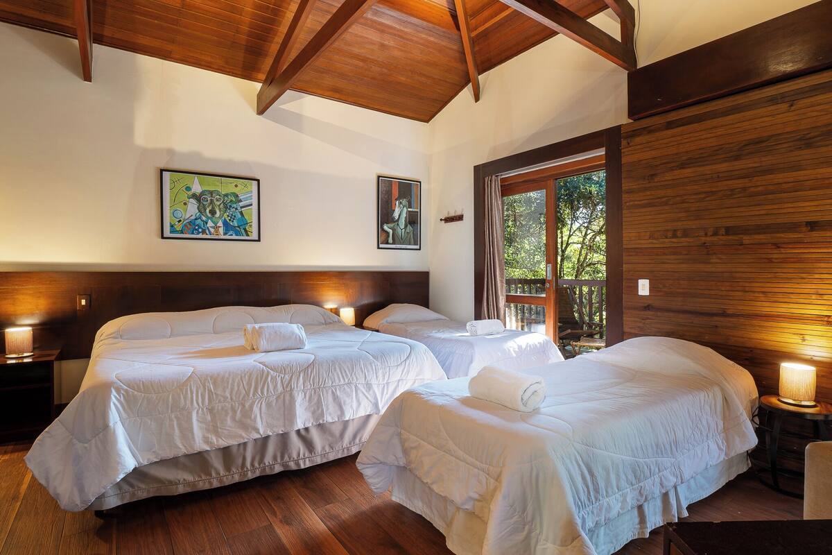 A room with three beds, wooden ceiling beams, and two wall-mounted paintings.