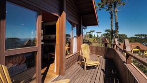 A wooden deck with a wooden chair and a table, overlooking a scenic landscape with trees and buildings.