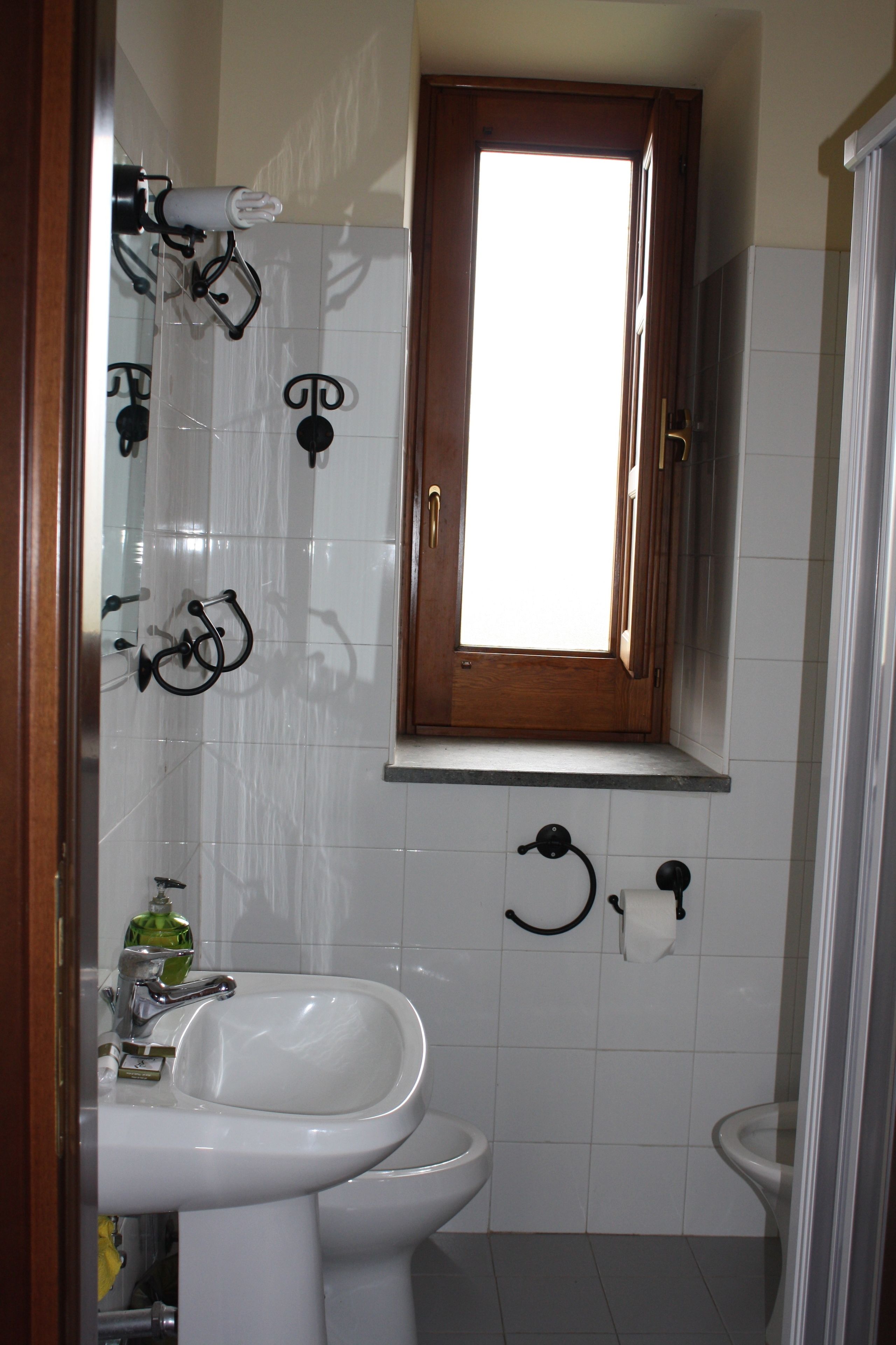 A bathroom with a window, a sink, a toilet, and a mirror.