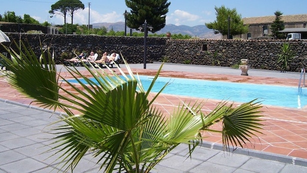 Piscina com espreguiçadeiras, cercada por muros de pedra e palmeiras.