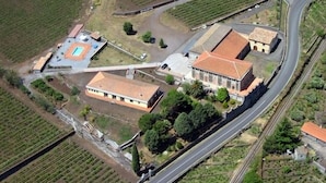 Vista aérea de uma propriedade com vários edifícios, piscina e campos agrícolas ao redor.