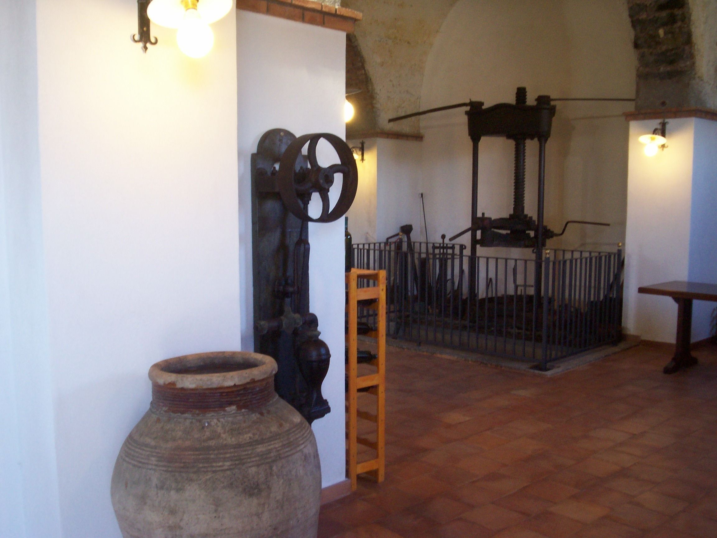 Ein rustikales Interieur mit einem großen Tonkrug, einer Holzleiter und einem Metallgitter.