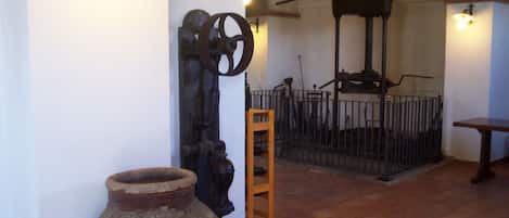 A rustic interior with a large clay pot, a wooden ladder, and a metal gate.
