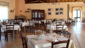 Uma ampla área de jantar com várias mesas e cadeiras, vigas de madeira no teto e um lustre.